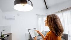 This image shows a young woman who controls the light in her smart home with a tablet.